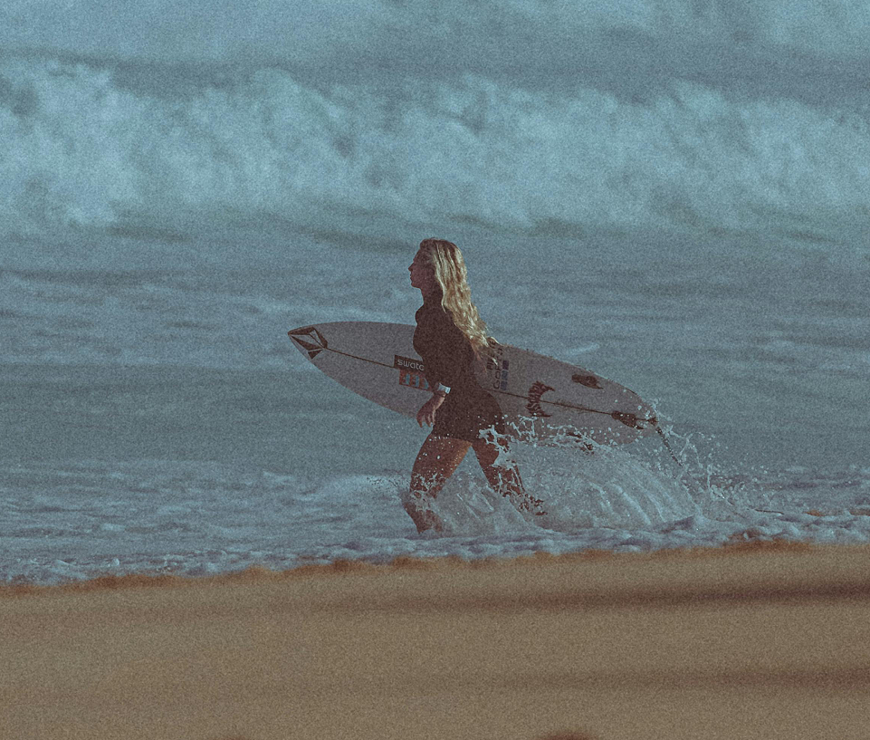 A surfer is walking into the ocean on his board.